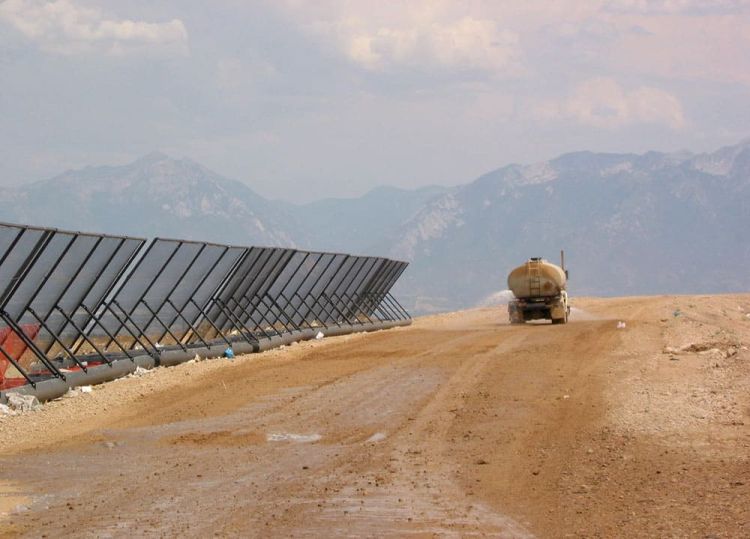 A water tanker truck drives along a dirt road next to a long row of Coastal Netting&rsquo;s portable litter fences. There are mountains visible in the background.