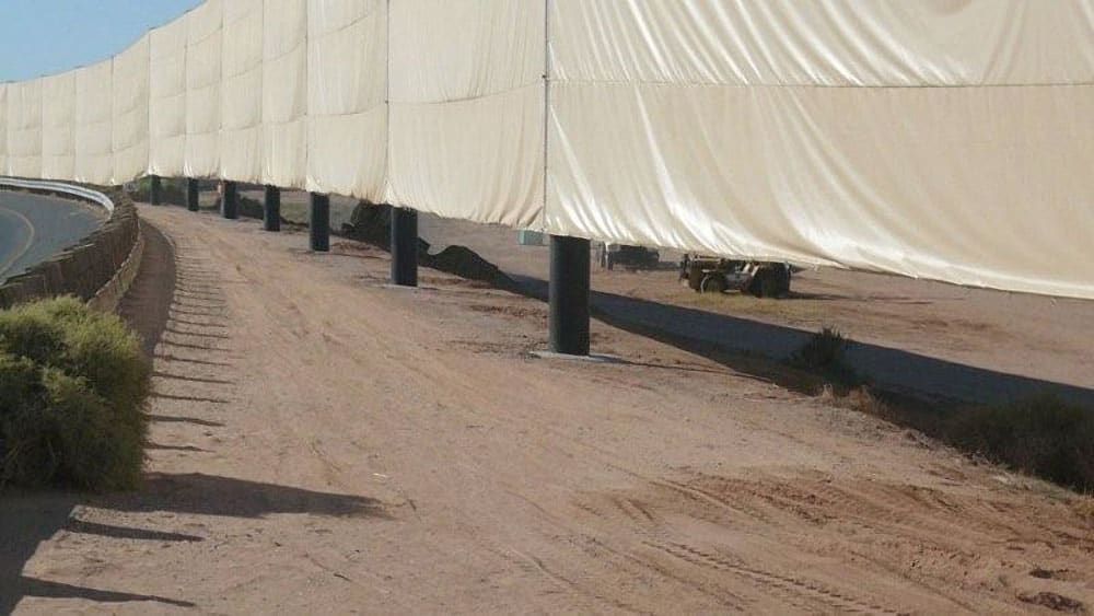 Large tan fabric panels are stretched and suspended on metal poles, providing a visual screen for what’s behind it from the nearby road.